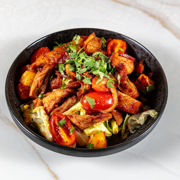 Spicy Thai salad with grilled chicken, cherry tomatoes, and fresh cilantro in a black bowl.