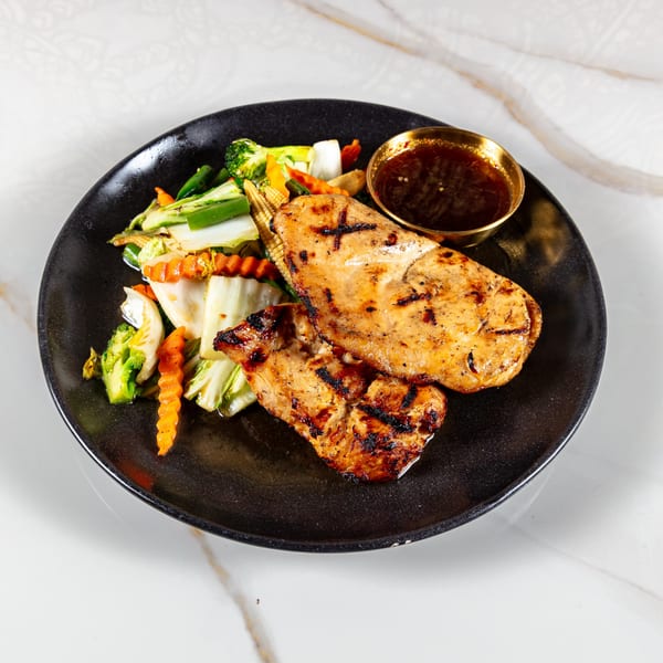 Grilled chicken breast with stir-fried vegetables and a side of sauce on a black plate.