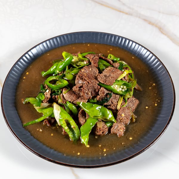 Slices of beef and green bell peppers in a brown sauce, served on a dark gray plate.